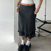 Person wearing a black patterned skirt with white socks and black shoes in an indoor setting.